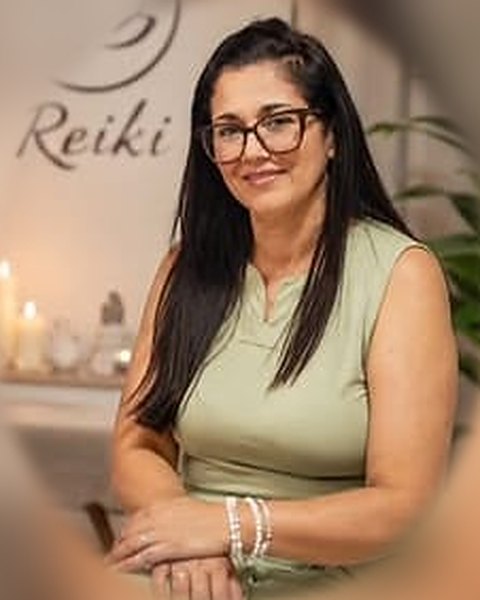 Retrato de Suzana Silvia, de óculos e vestido verde, em sala de Reiki