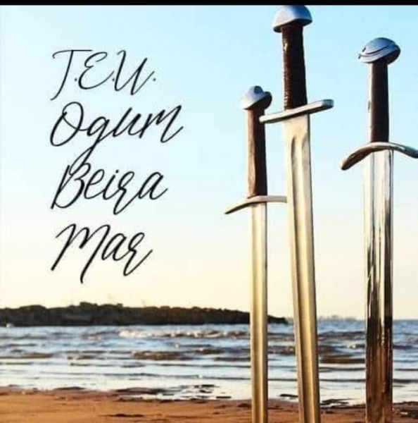 Espadas fincadas na areia à beira-mar ao entardecer, com a inscrição TEU Ogum Beira Mar